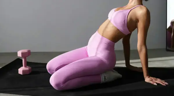 Kobieta w różowych legginsach plus size z wysokim stanem i dopasowanym biustonoszem ćwiczy na macie obok różowego hantla.