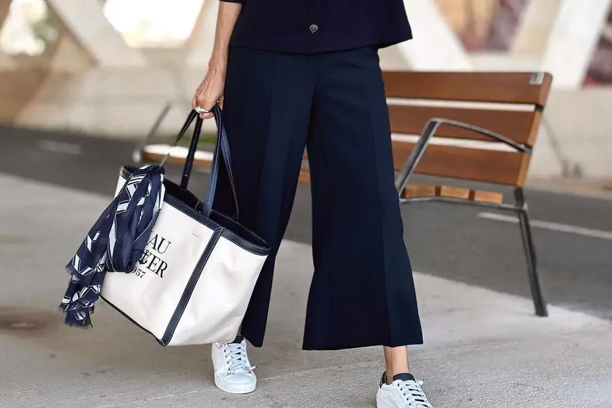 Eleganckie kuloty plus size w granatowym kolorze, biała torba z granatowym napisem i apaszka, białe sneakersy.